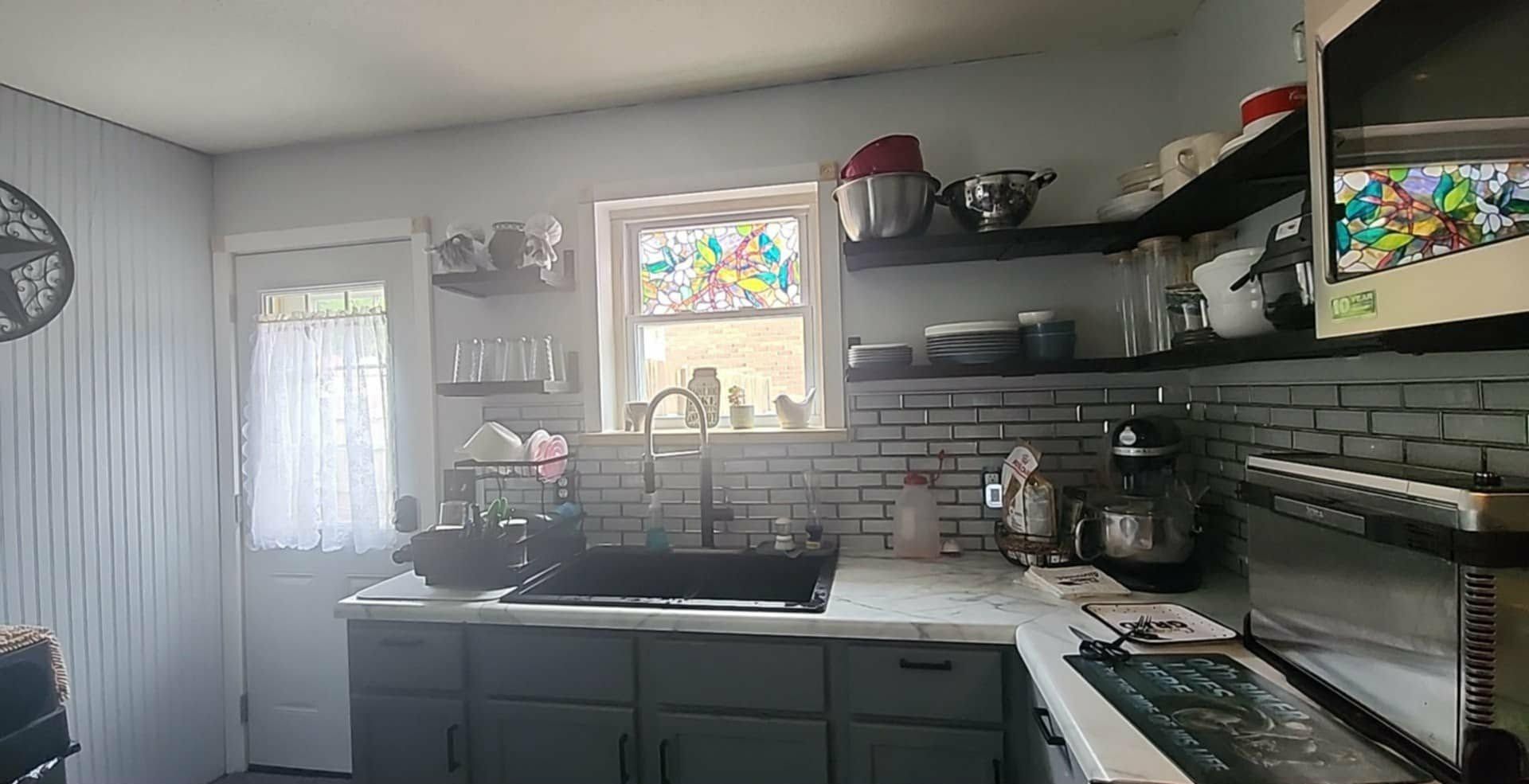 Modern kitchen with green cabinets, white countertops, brick backsplash, and a sink under a window.