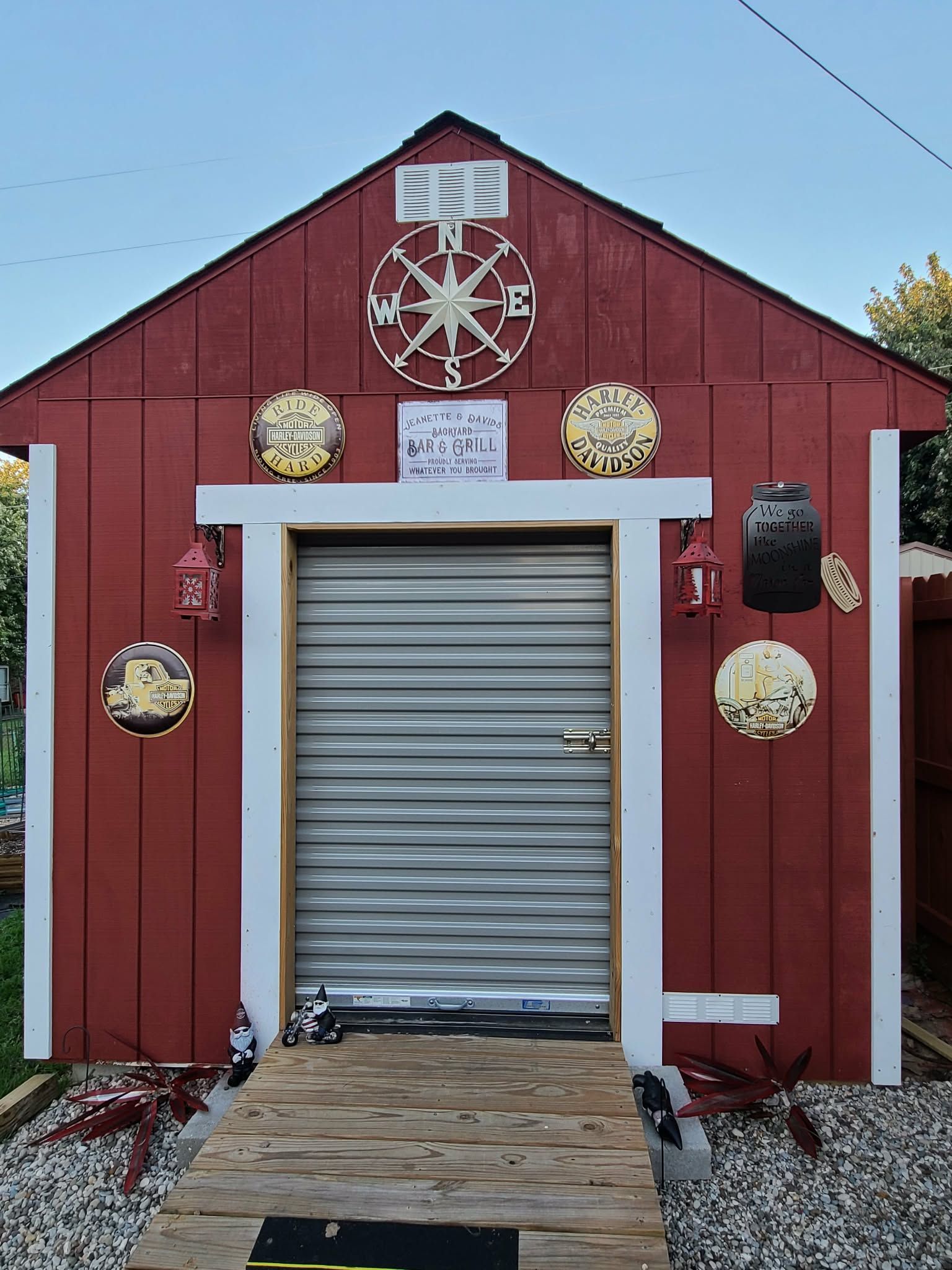Red shed with white trim, metal roll-up door, and nautical wall decor on a gravel lot