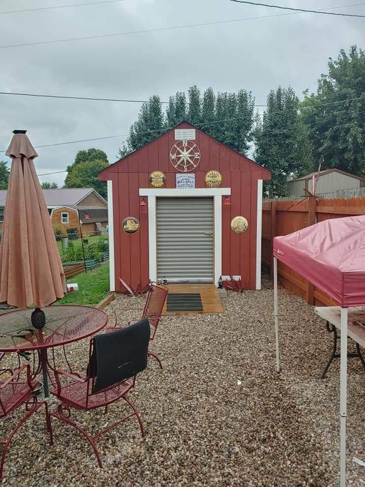 Red backyard shed with a roll-up door, gravel patio, and outdoor furniture under an overcast sky