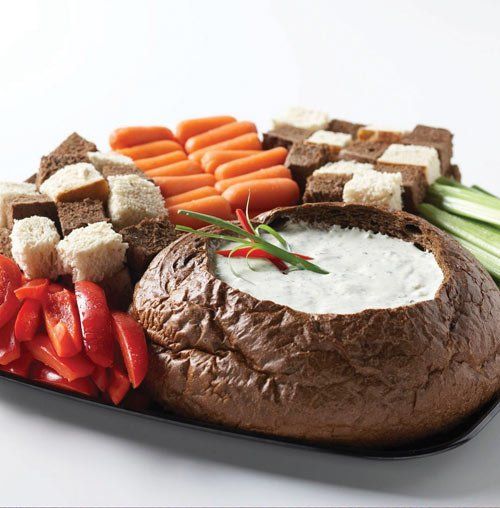 Assorted vegetables and bread arranged around a spinach dip bowl on a serving tray