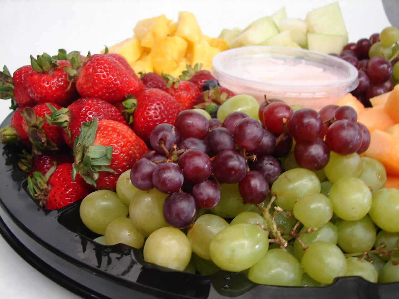 Assorted fresh fruit platter with strawberries, grapes, melon, and dip on a serving tray