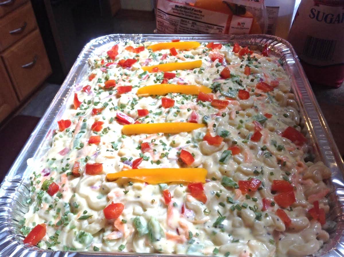 Tray of creamy pasta salad topped with cherry tomatoes, parsley, and yellow bell pepper strips