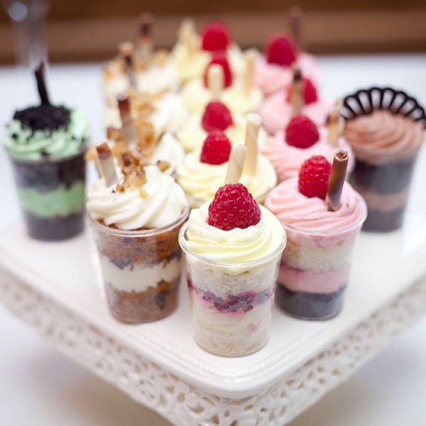 Assorted layered dessert cups topped with whipped cream and berries on a white serving tray