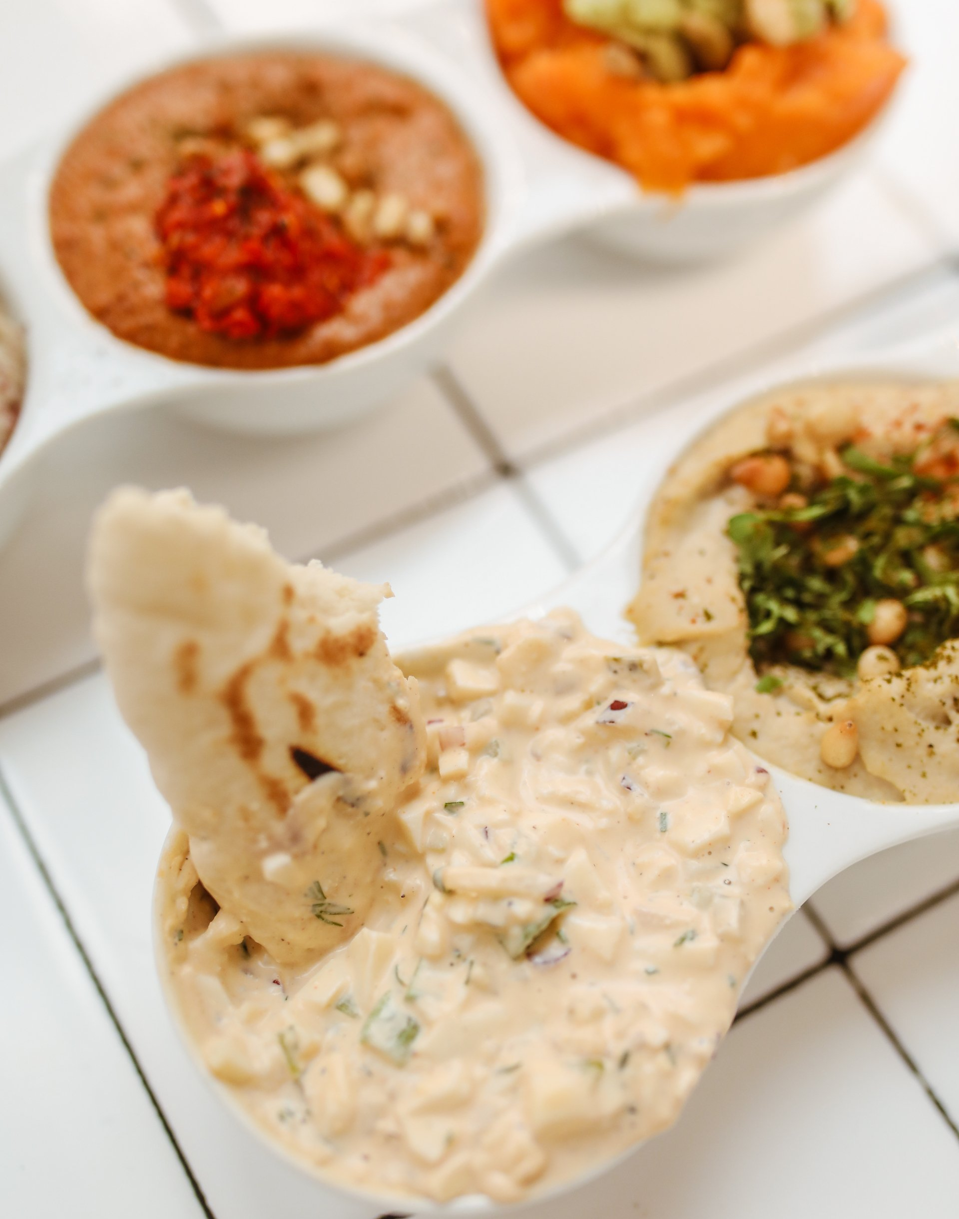 Three bowls of colorful Indian chutneys and dip with a crisp papad in front.