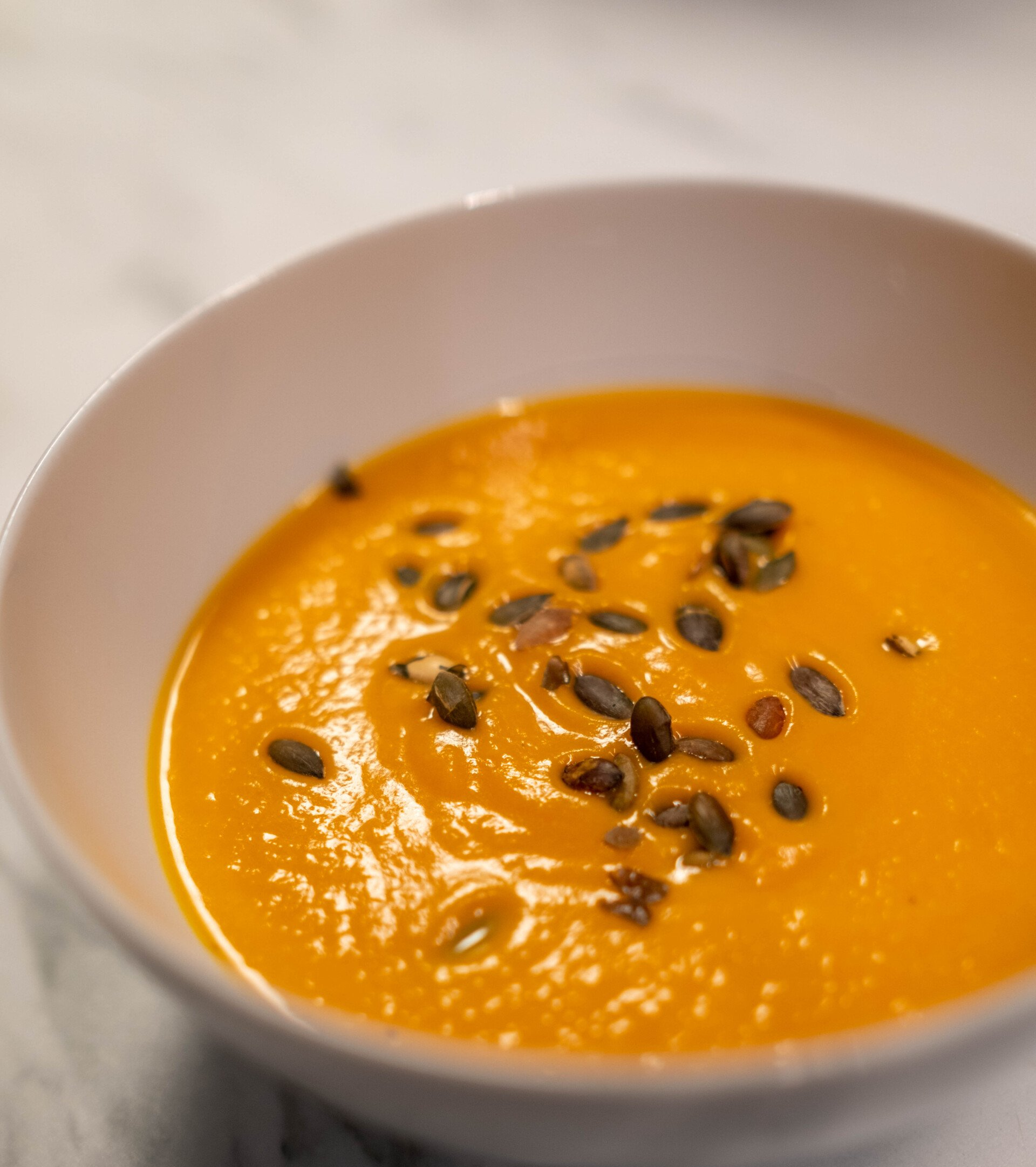 Orange soup garnished with pumpkin seeds in a white bowl