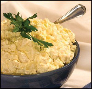 Creamy potato salad in a blue bowl, garnished with parsley and a serving spoon