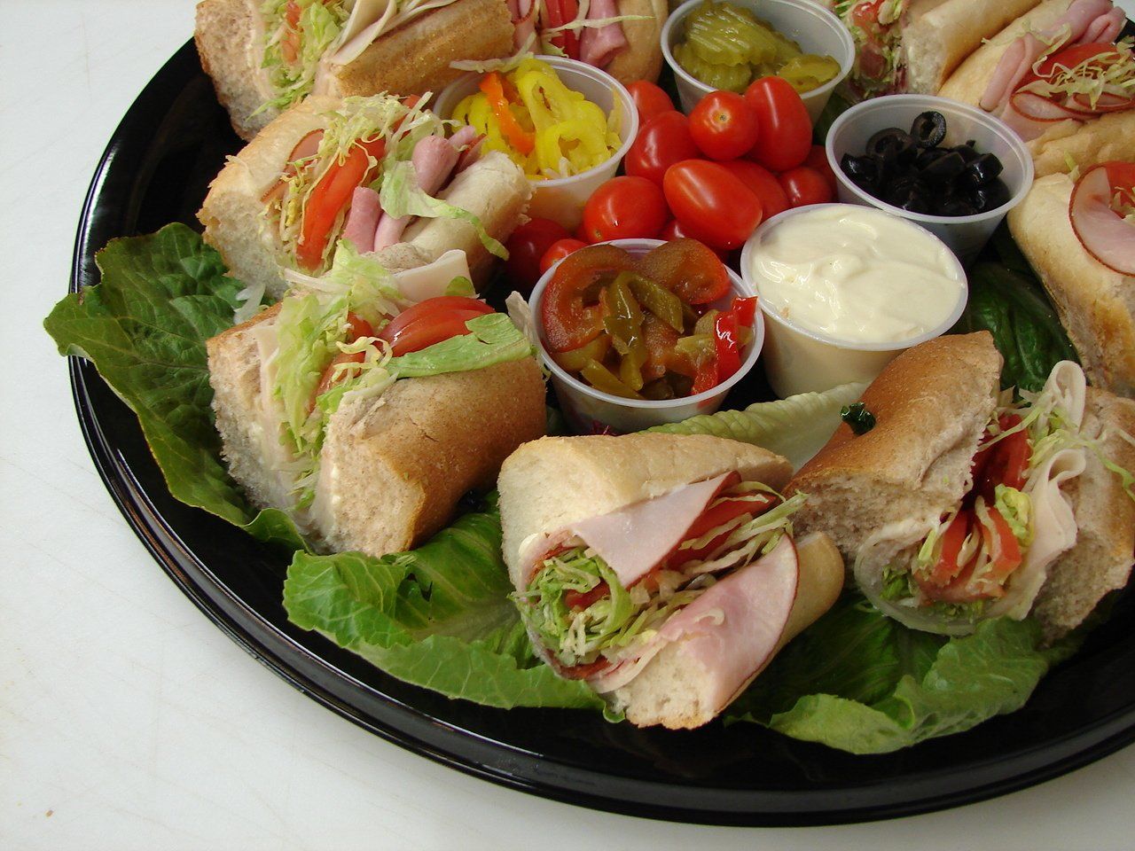 Club sandwich platter with lettuce, tomatoes, cherry tomatoes, pickles, and dipping sauces