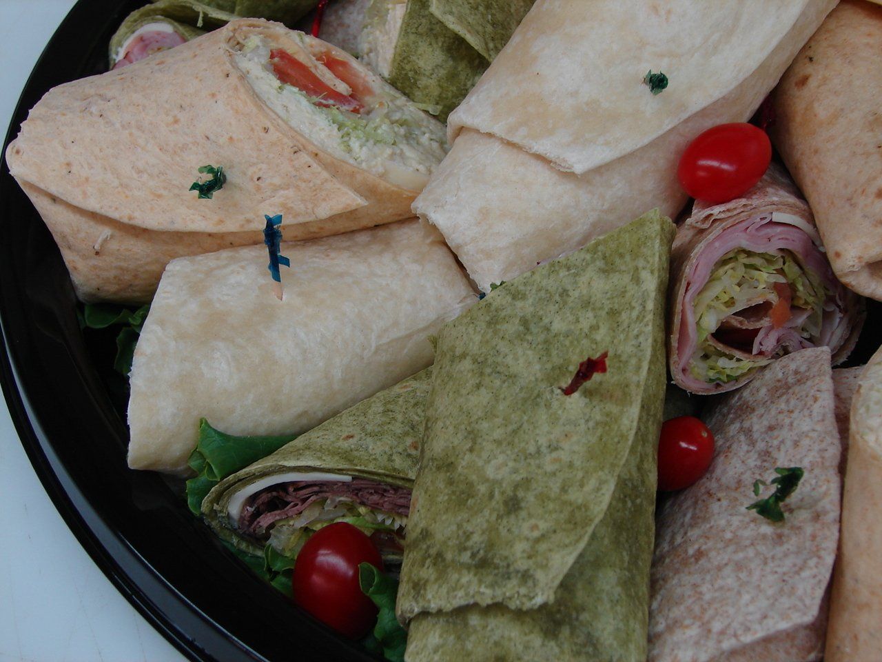 Assorted wrap sandwiches with lettuce, meat, and cherry tomatoes in a black bowl