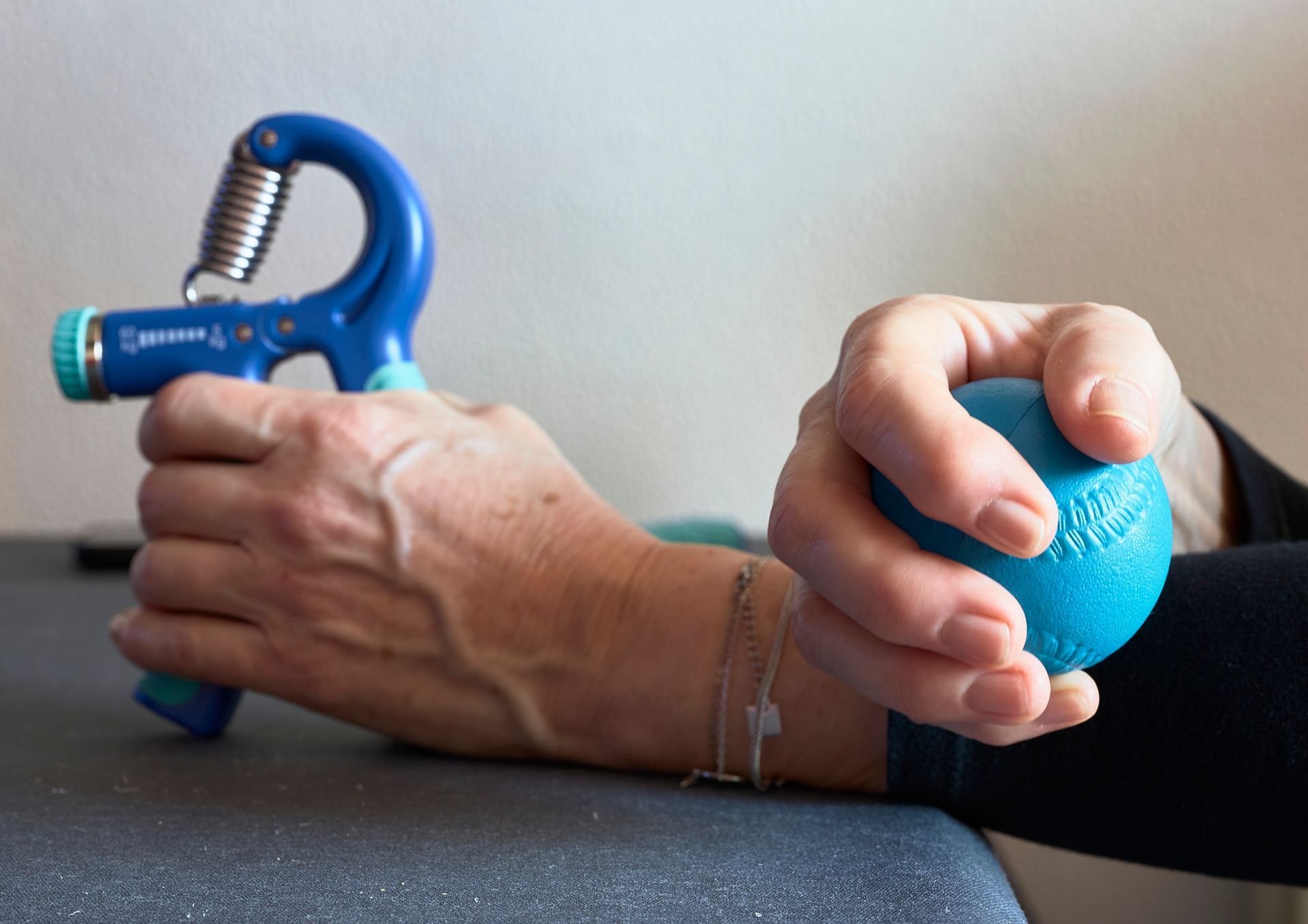 Person squeezing a blue hand exerciser and a blue stress ball on a table.