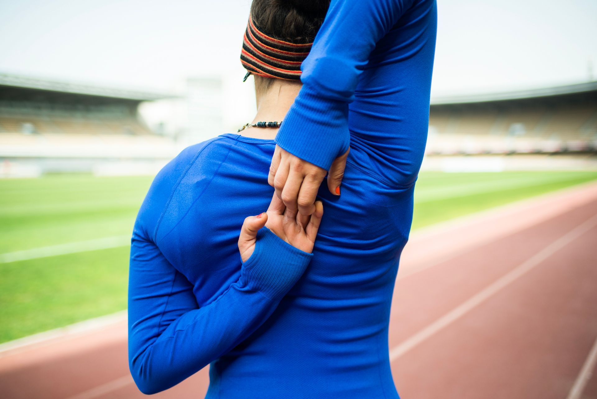Woman in blue stretching arm behind her back on a track field.