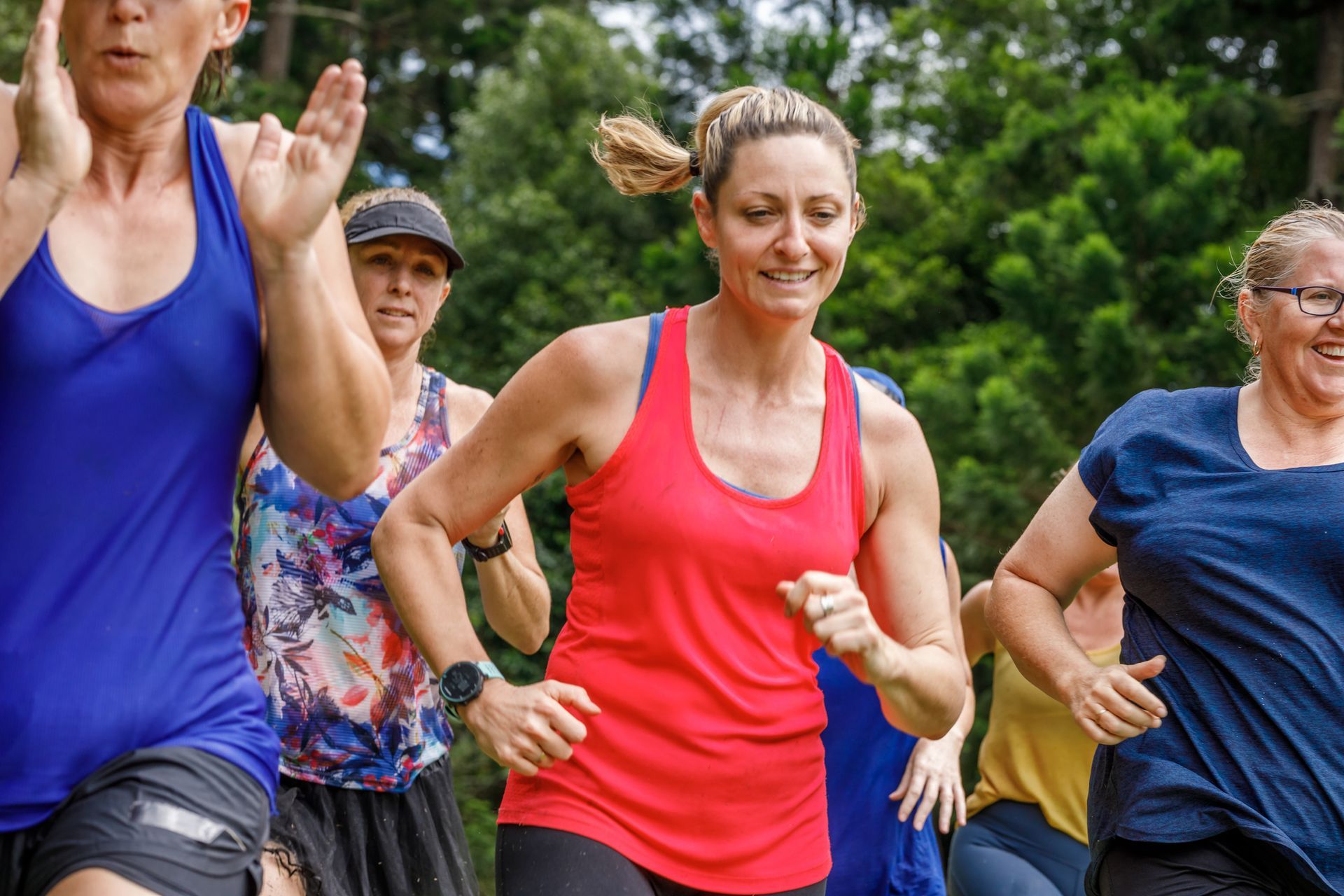Group of people running outdoors; woman in red tank top smiles, others follow.