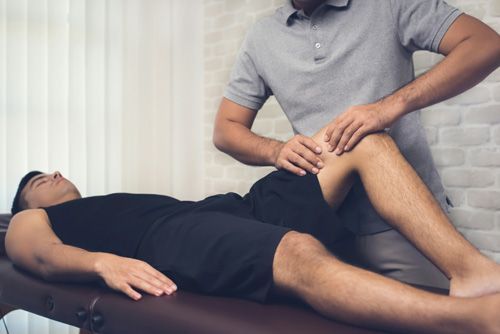 Man receiving physical therapy on his knee; therapist manipulating leg.