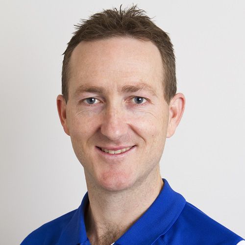 Man in blue polo shirt smiling, neutral background.
