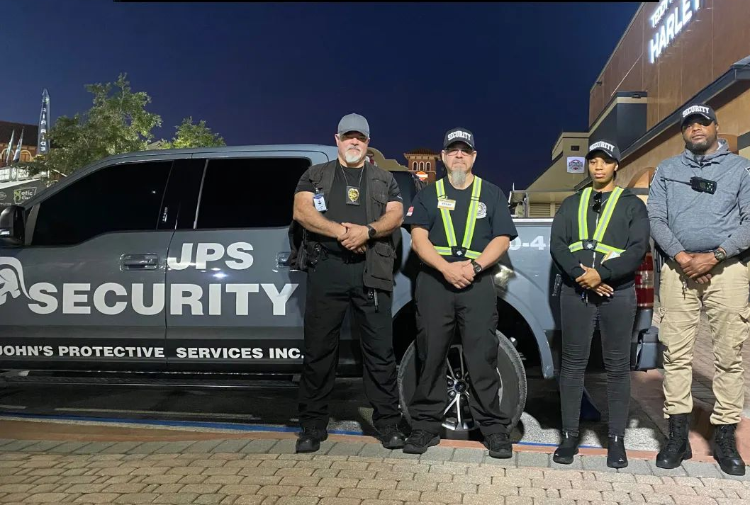 Security personnel standing in front of a security vehicle, nighttime setting. The vehicle displays