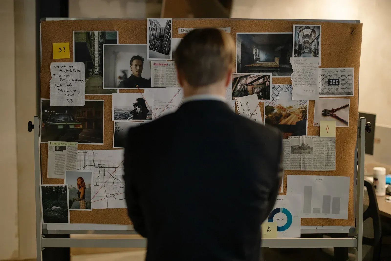 Person studying a bulletin board covered with notes, photos, and newspaper clippings.