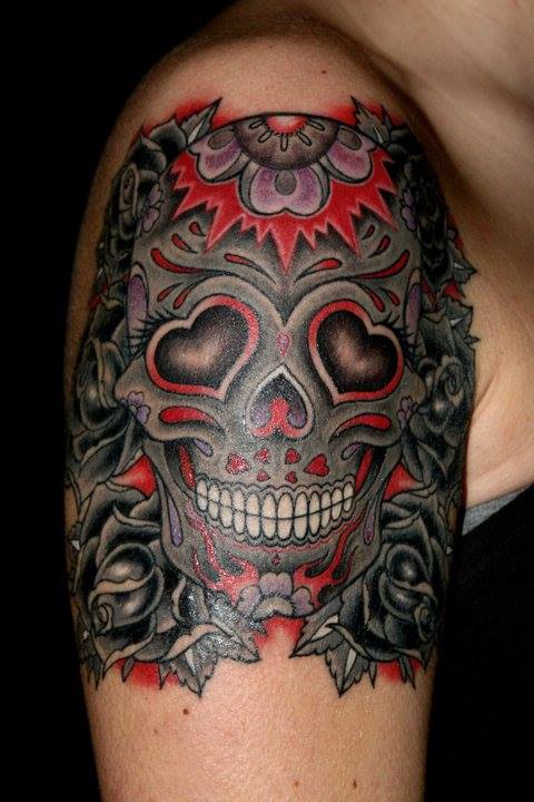 Close-up of a colorful skull tattoo with red, black, and gray floral details on an upper arm