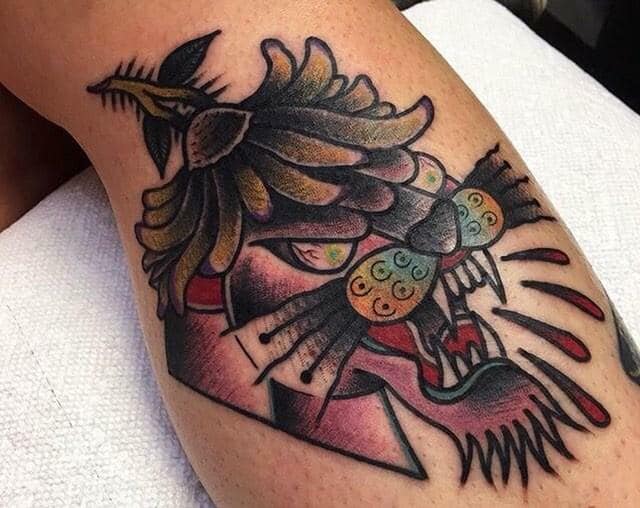 Colorful bird and floral tattoo on skin with black outlines and pink, green, and orange details