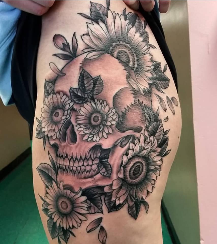Black and gray skull tattoo with flowers on a person’s side torso