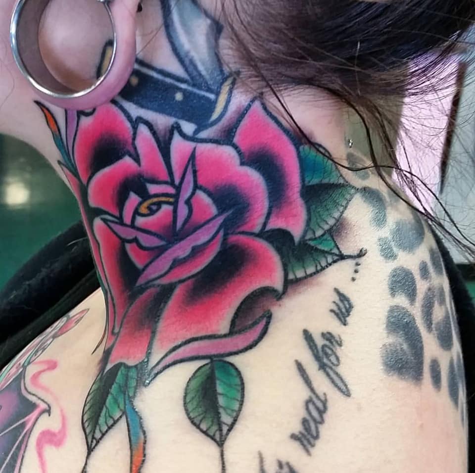 Close-up of a neck tattoo featuring a pink rose with green leaves and black script text, next to an ear gauge