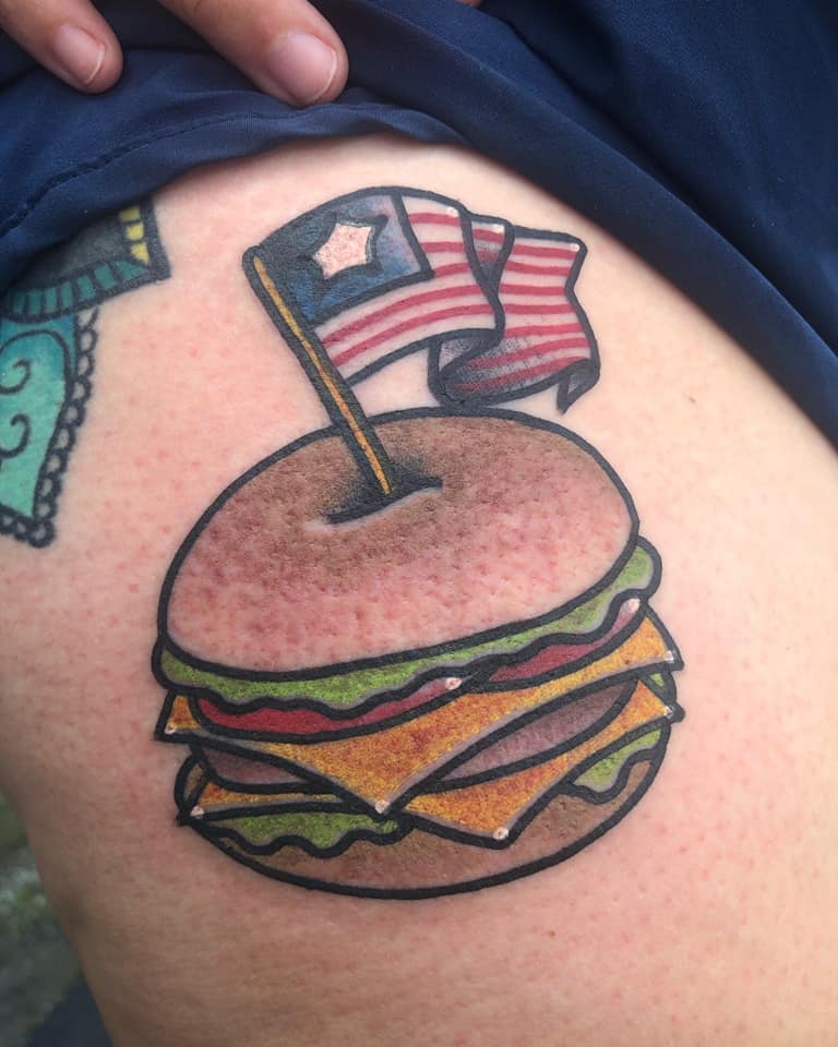 A tattoo of a hamburger with a small American flag on top.