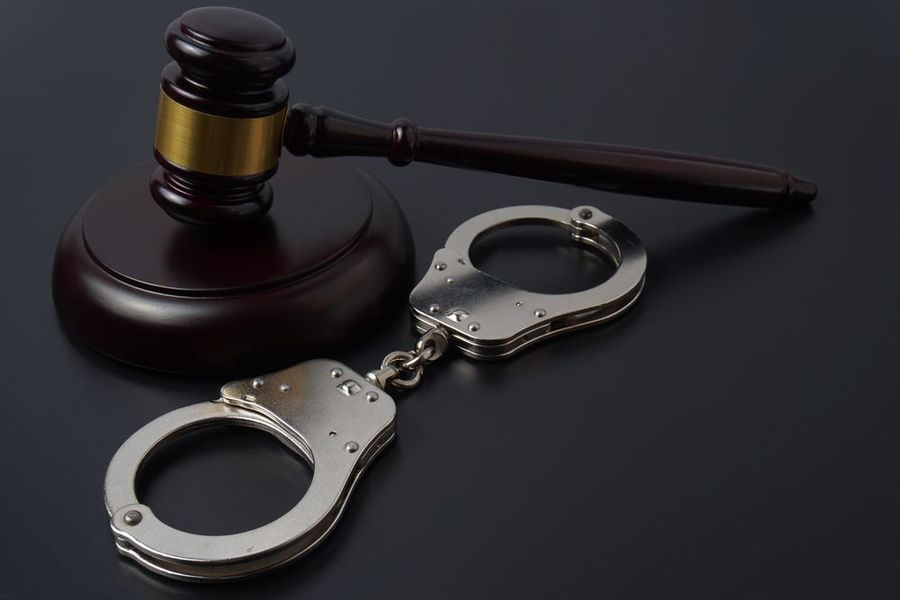 A wooden judge's gavel resting on its sounding block next to a pair of metal handcuffs against a dark background.