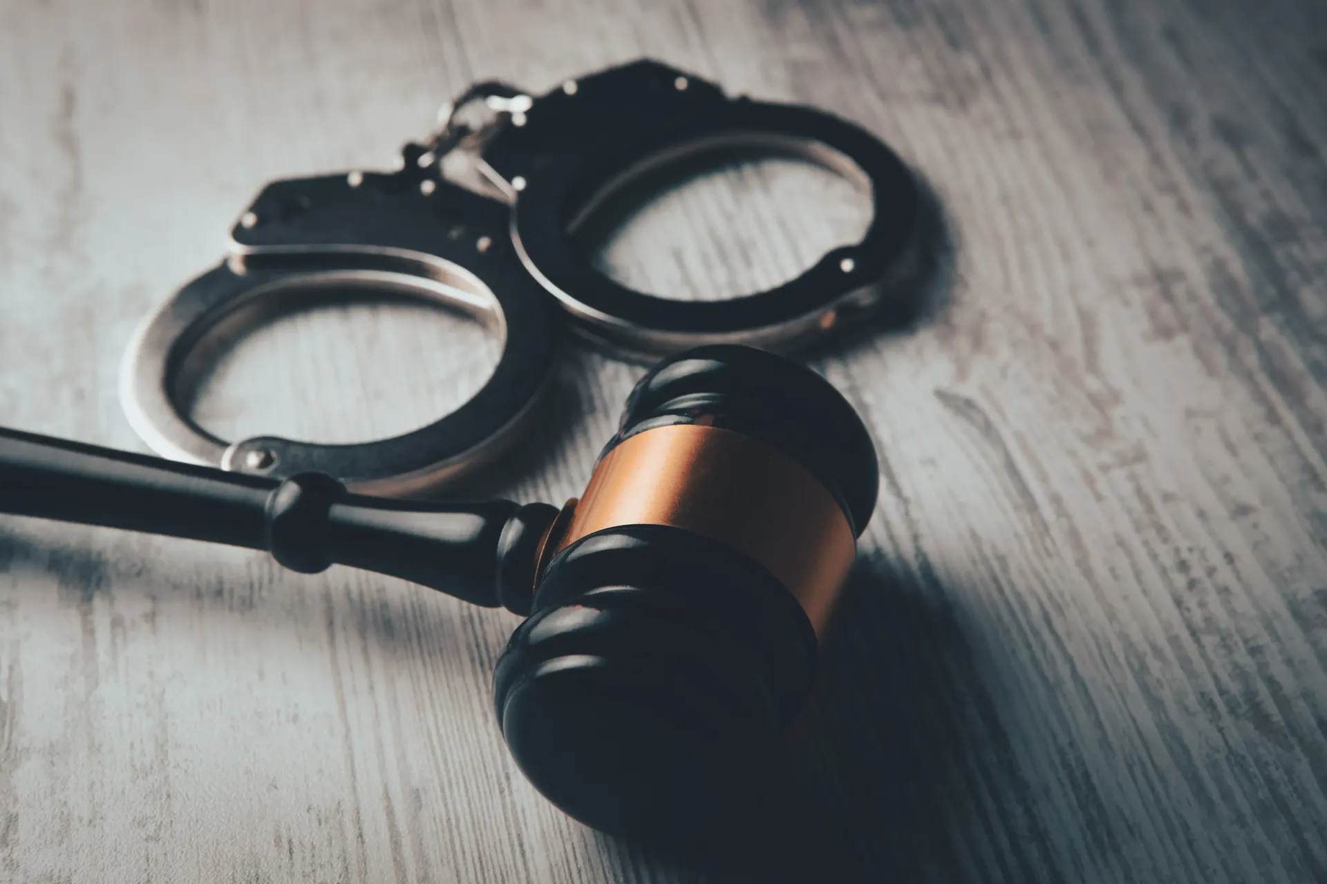A wooden judge's gavel resting next to a pair of metal handcuffs on a light gray wooden surface.