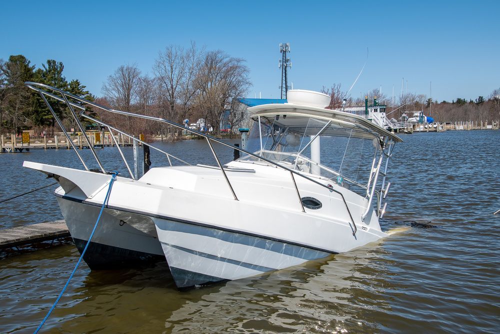 A white catamaran powerboat moored to a wooden dock on a calm lake under a clear blue sky.