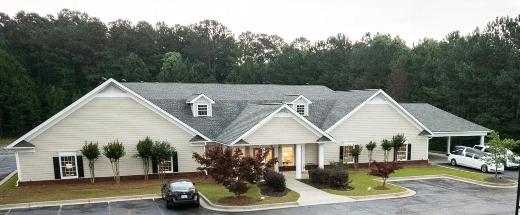 Single-story beige office building with a central entrance, parked car, and wooded backdrop