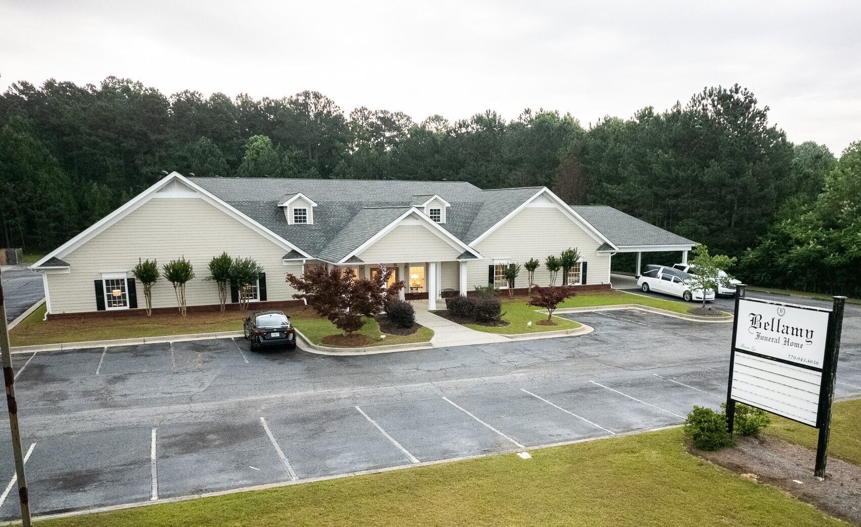 Single-story white office building with parking lot and sign in front, surrounded by trees