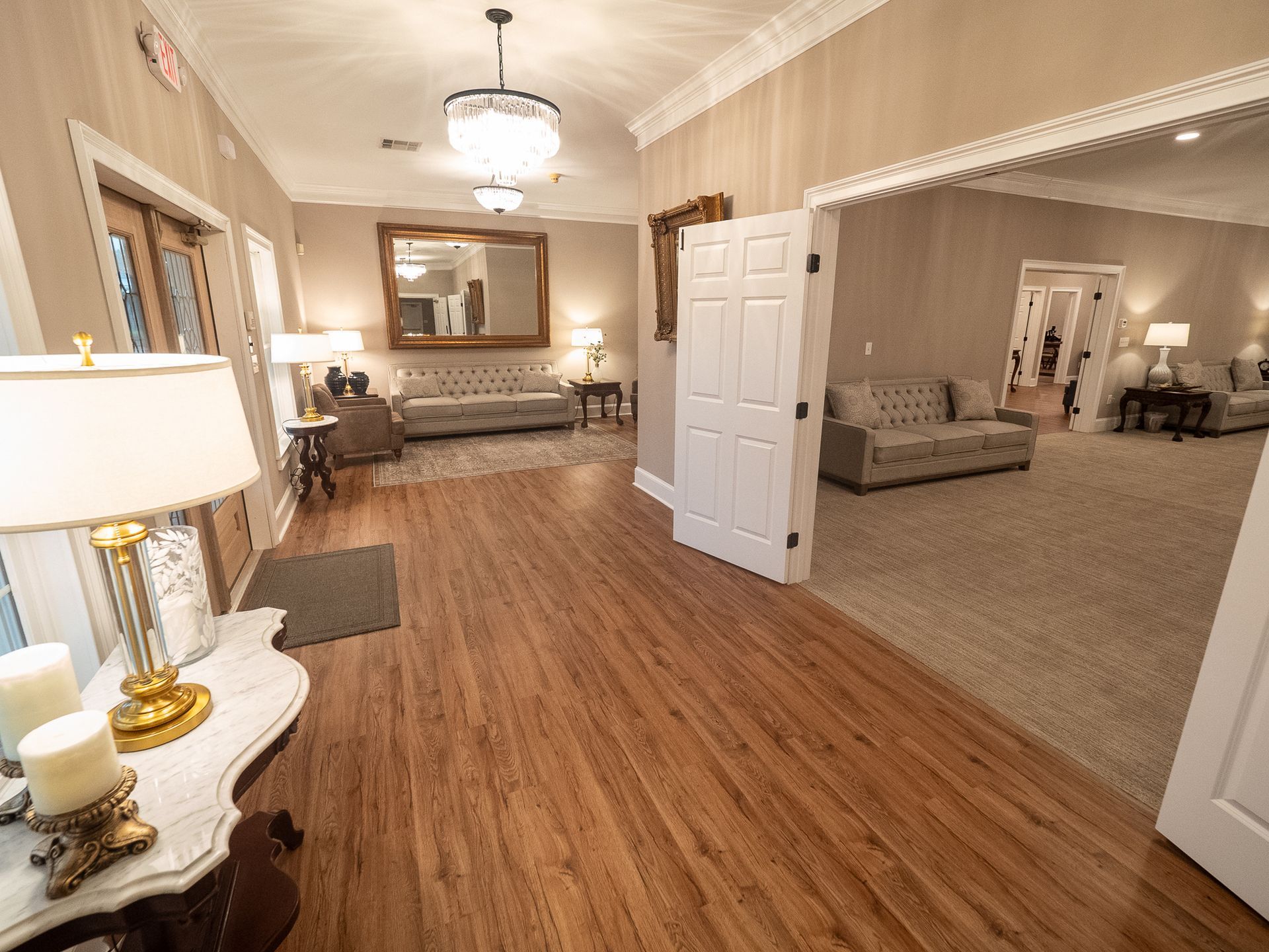 Bright hallway and living room with wood floors, beige walls, white doors, and a sofa in the adjoining room