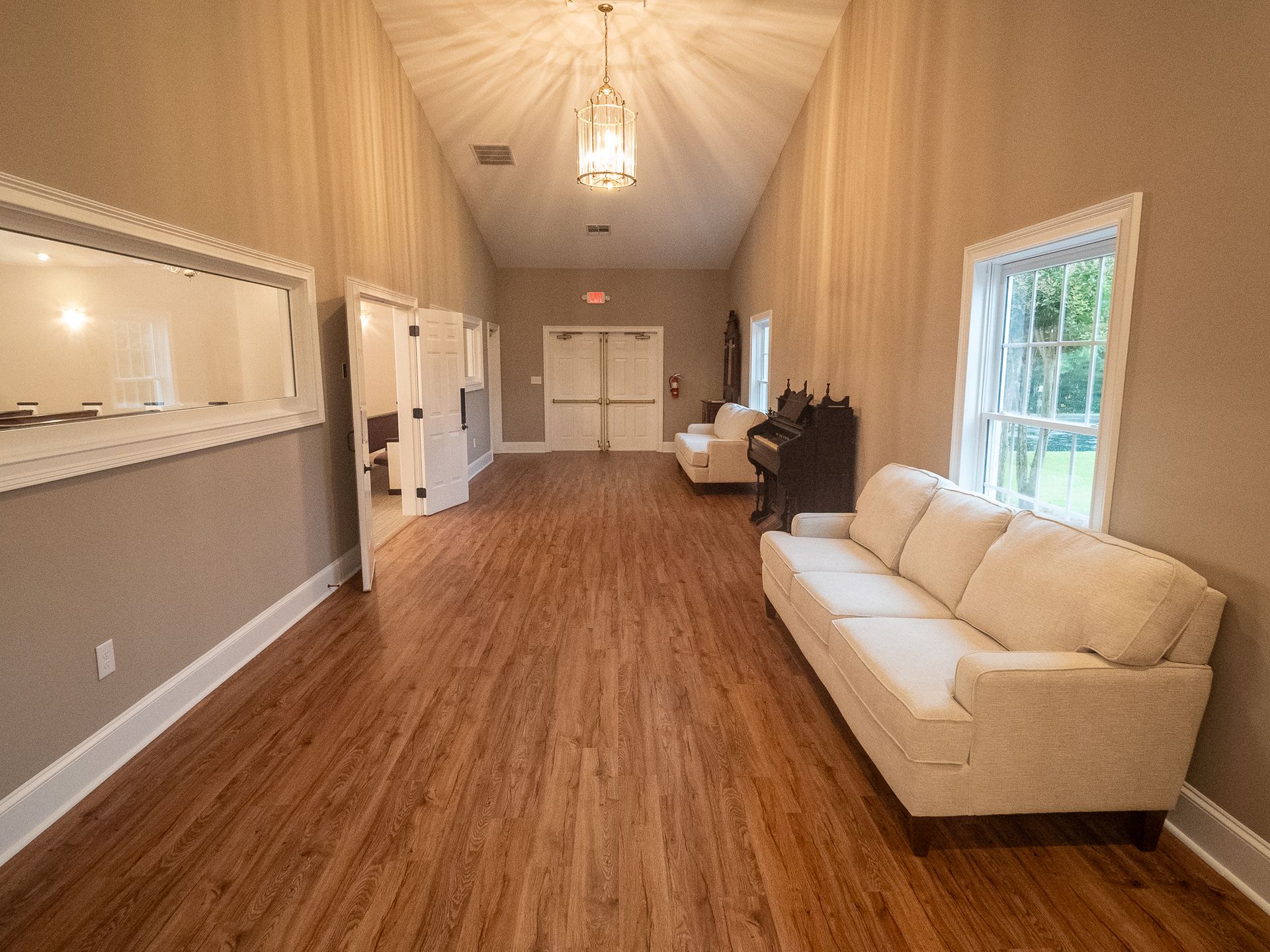 Bright, empty living room with wood floors, beige walls, white sofas, and large windows.