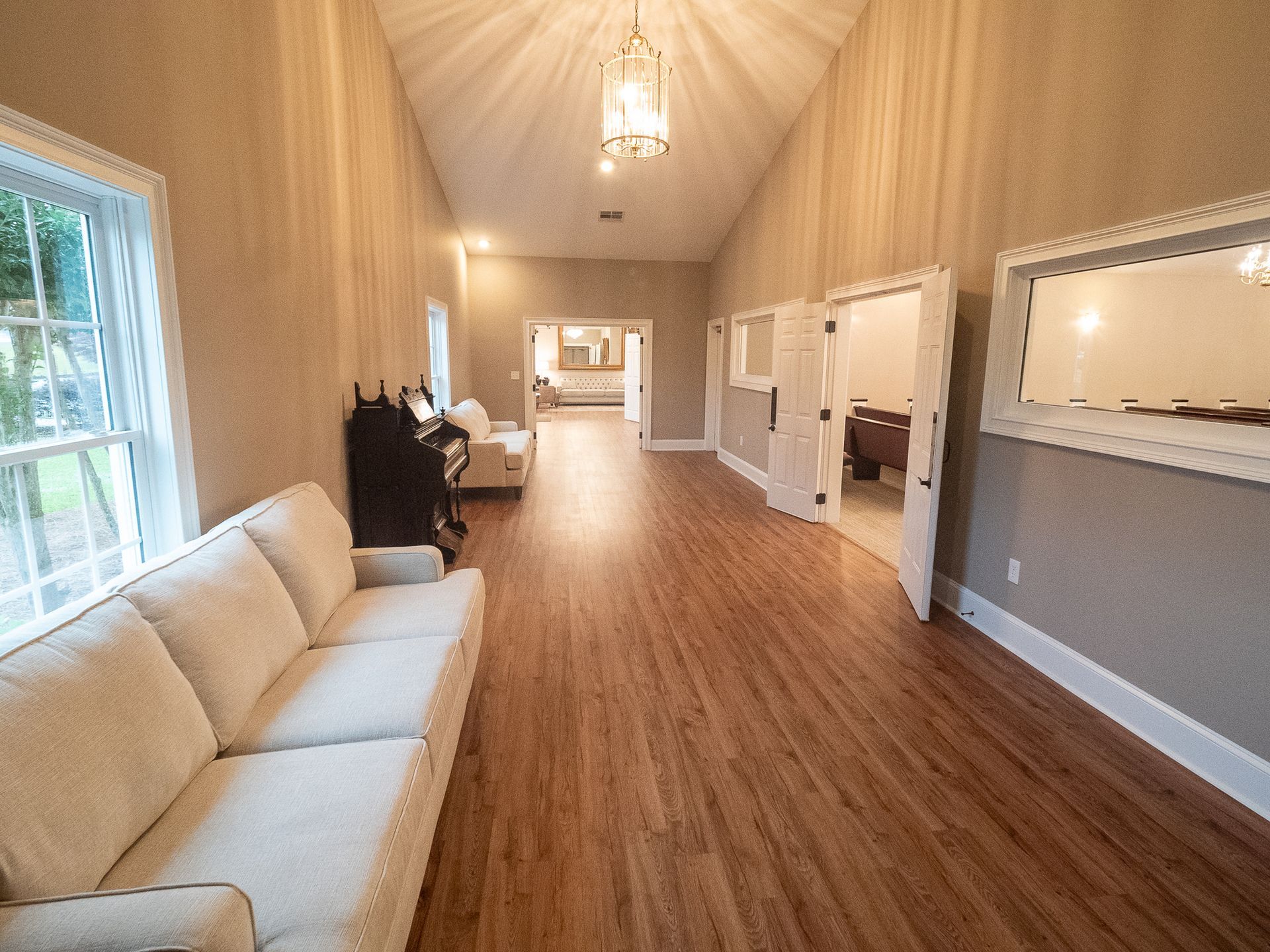 Long narrow waiting room with beige sofa, wood floors, high ceiling, and windows on the left.