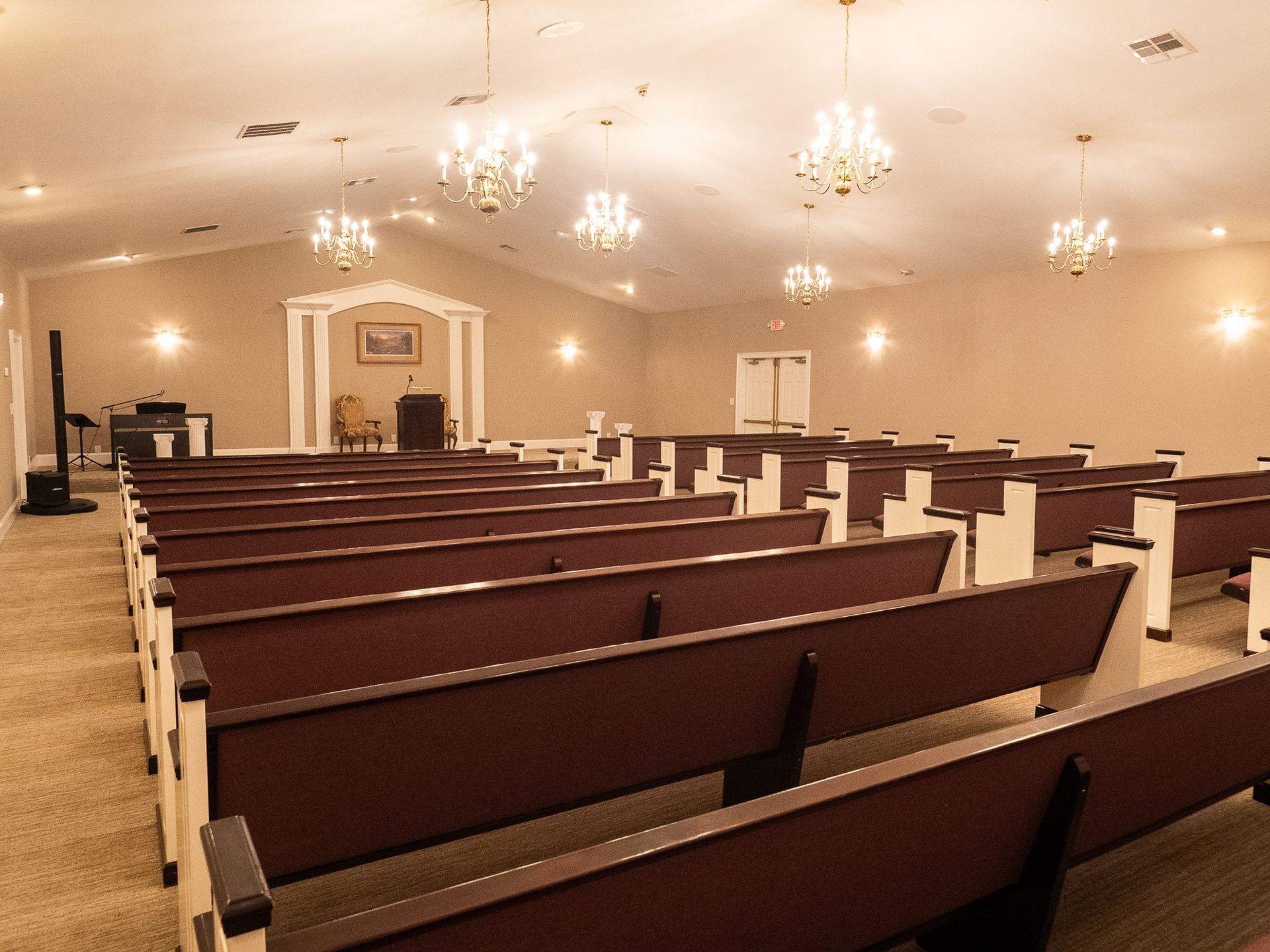 Empty church sanctuary with wooden pews, chandeliers, and a pulpit under warm lighting