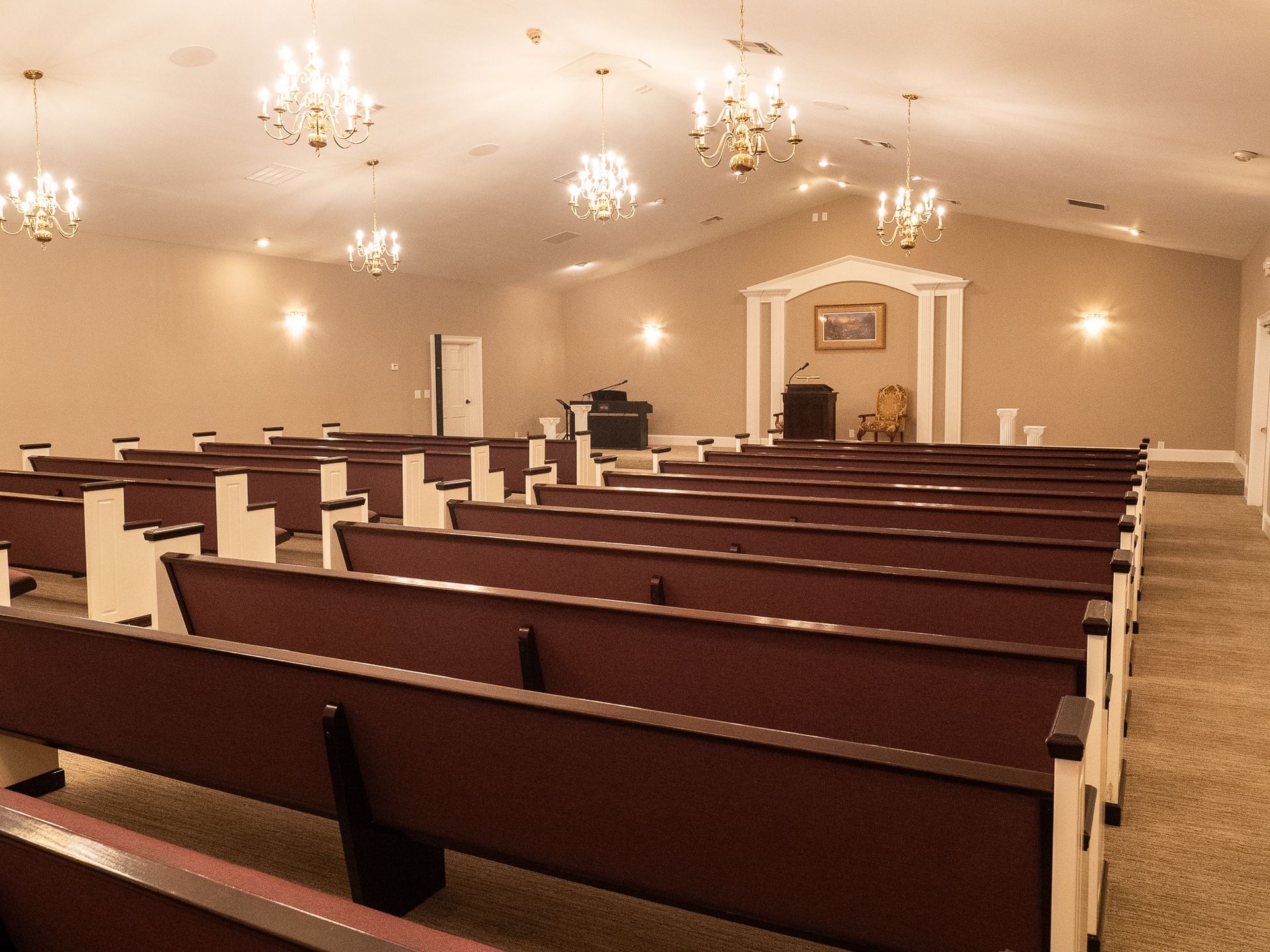 Empty church sanctuary with rows of wooden pews, chandeliers, and a pulpit at the front