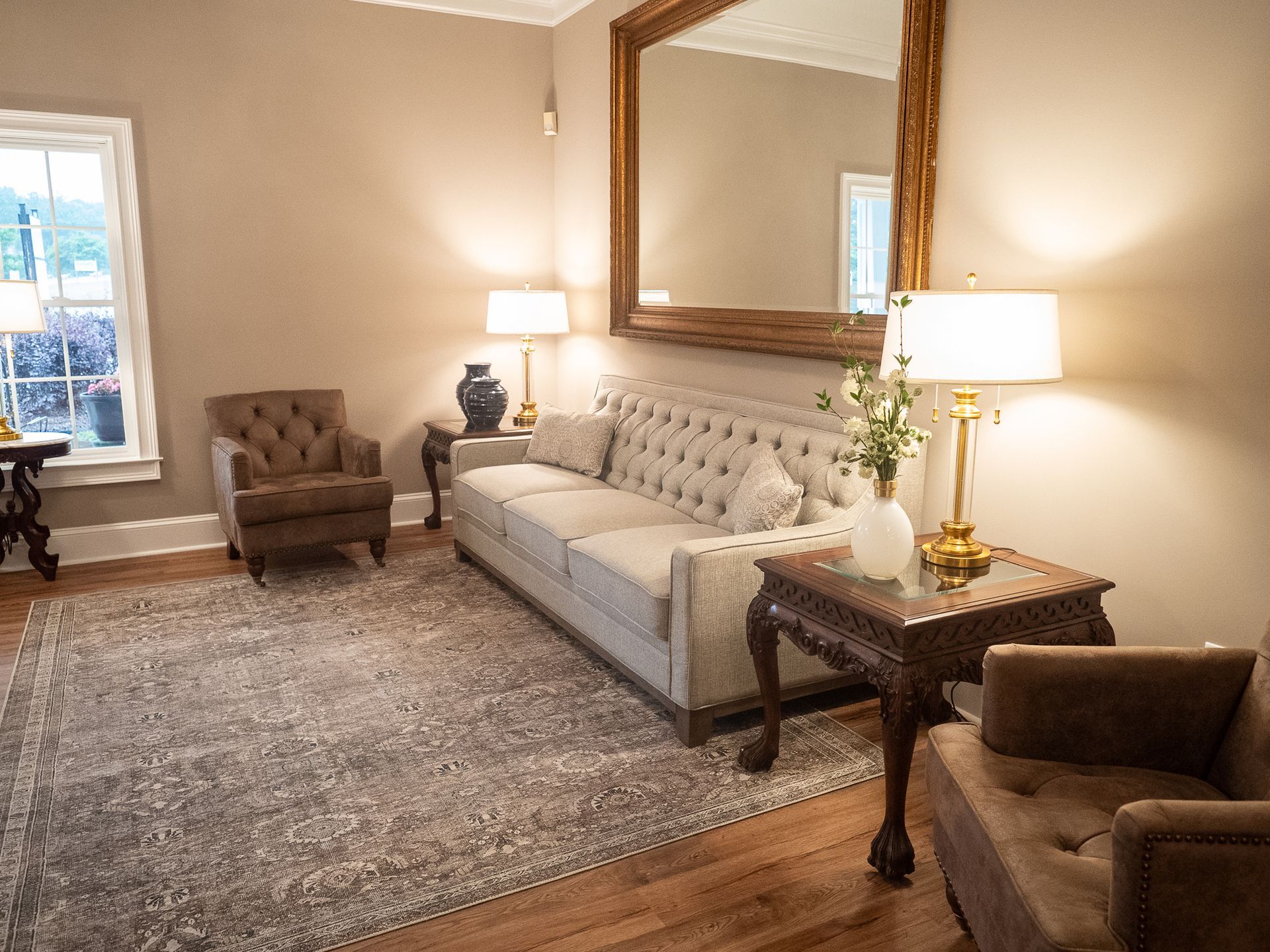 Cozy living room with beige sofa, armchairs, lamps, and a large wall mirror on neutral walls.