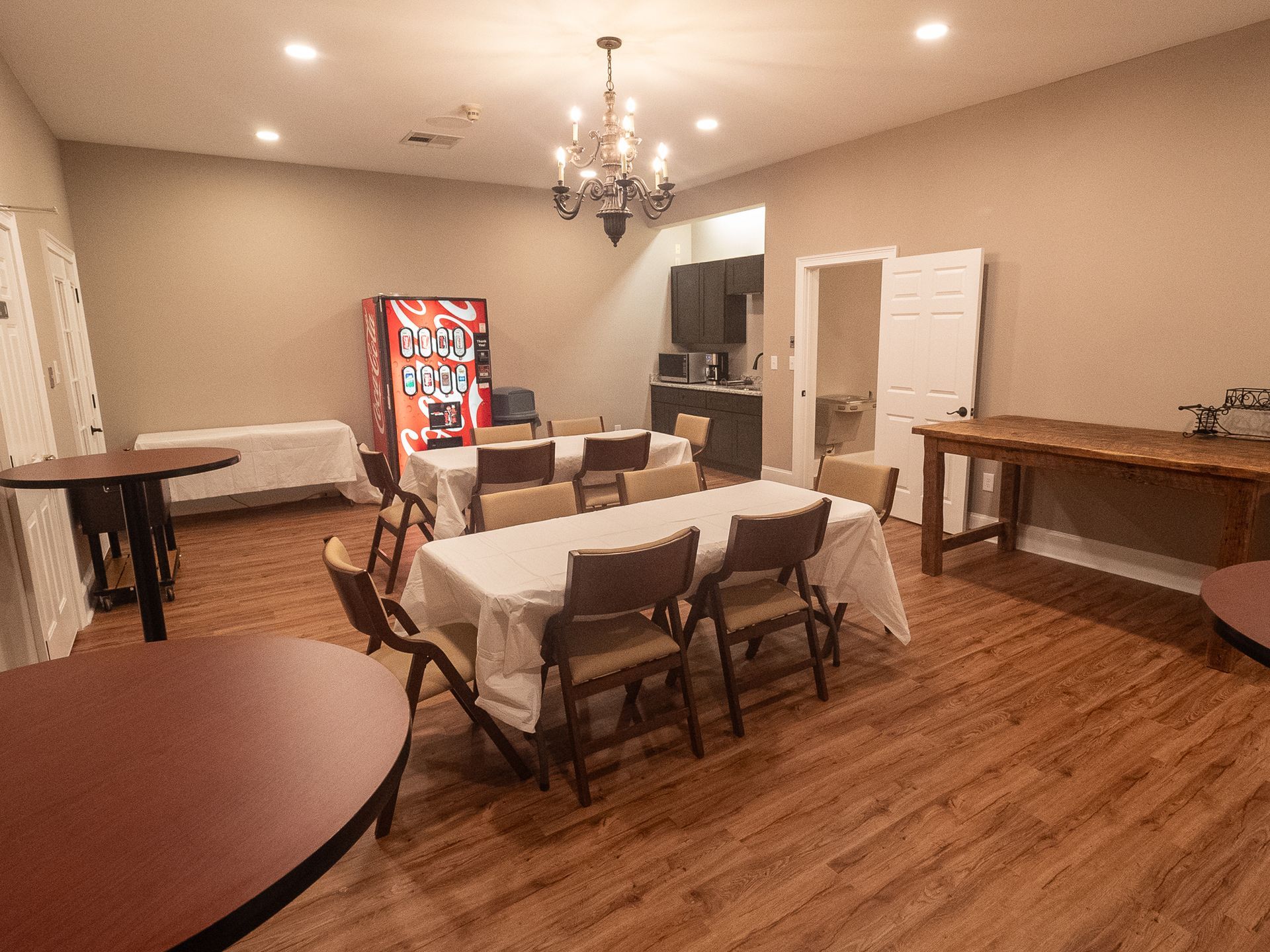 Banquet room with tables, folding chairs, a chandelier, and a red vending machine against beige walls.