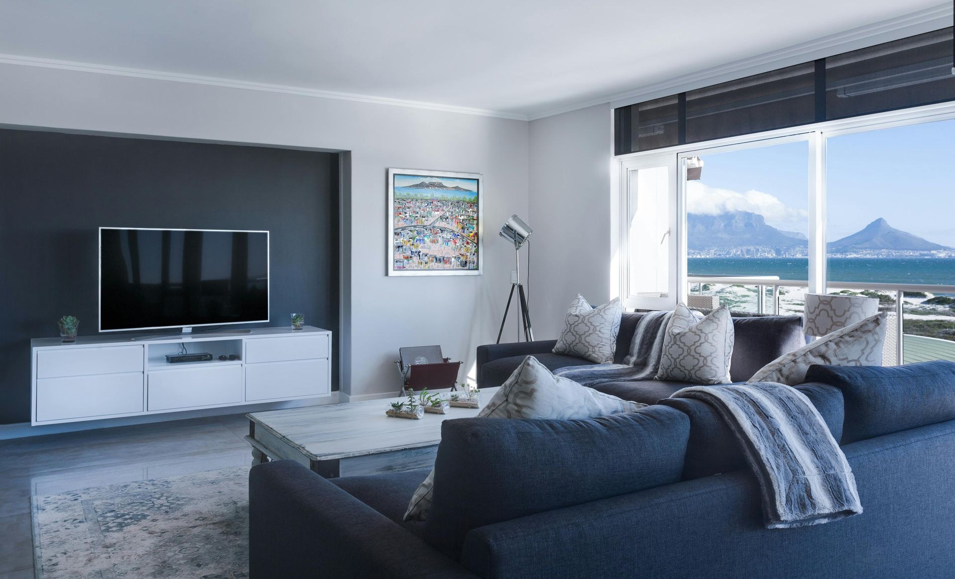 Living room with a dark blue sectional, TV, and window with a beach view.