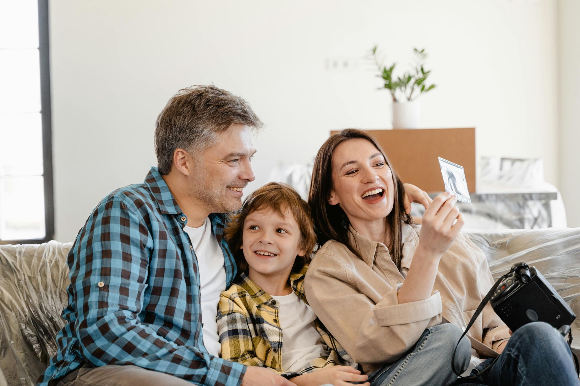 Family laughs while looking at a photo together on a sofa in a new home with moving boxes.