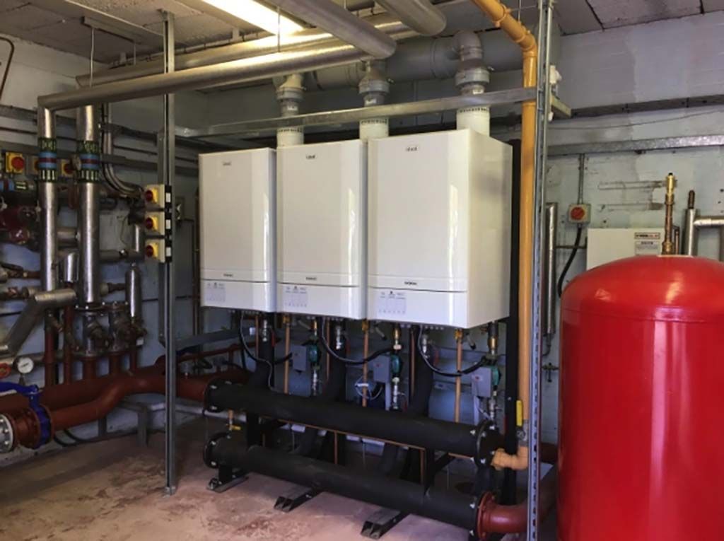 Three white wall-mounted boilers, with pipes, and a red tank in an industrial setting.