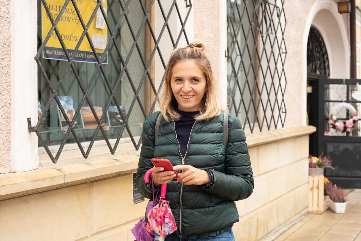 Женщина стоит перед зданием, держа в руках мобильный телефон.