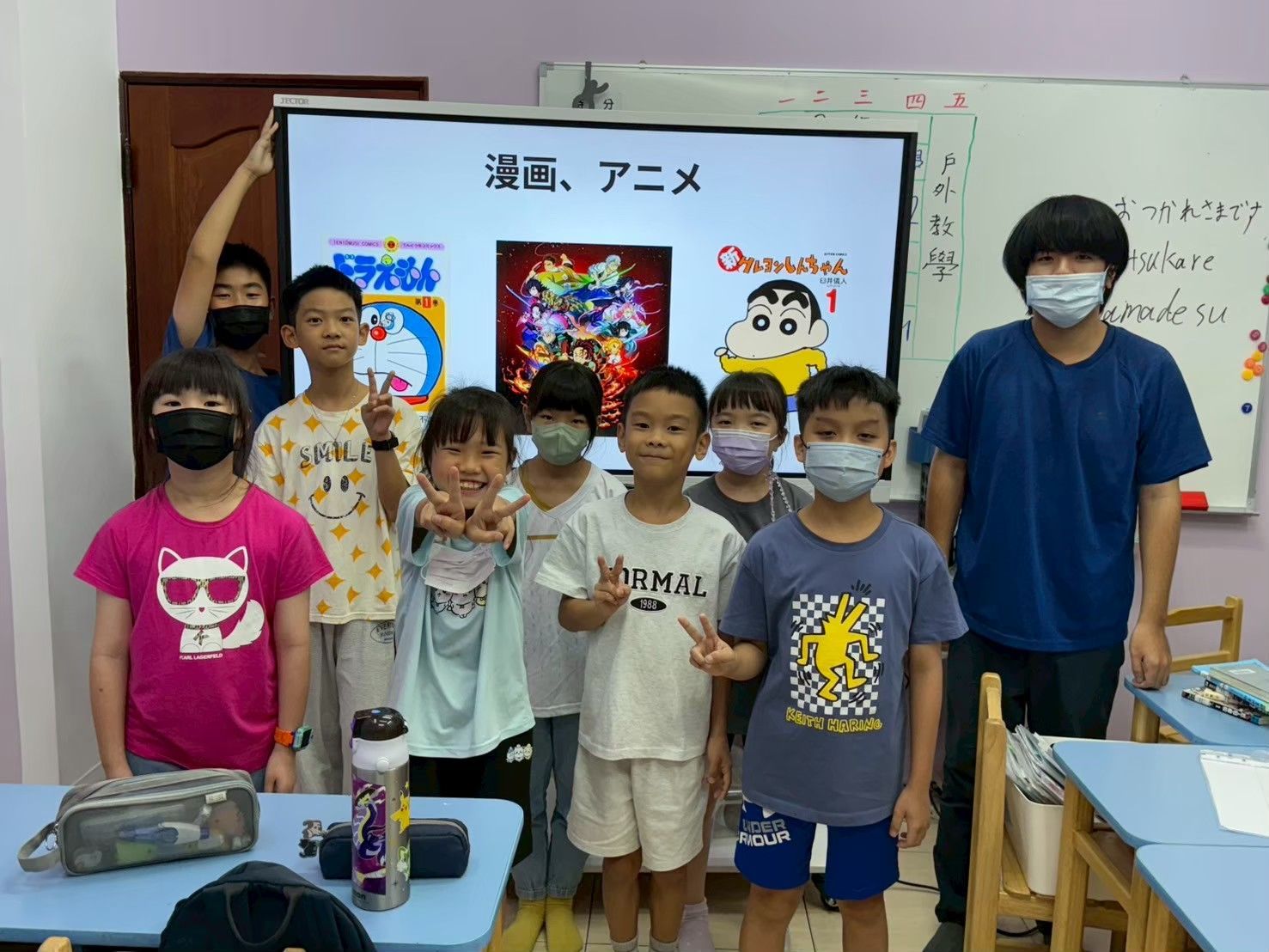 一群孩子和一位老師在教室裡,螢幕上播放著日本動漫。