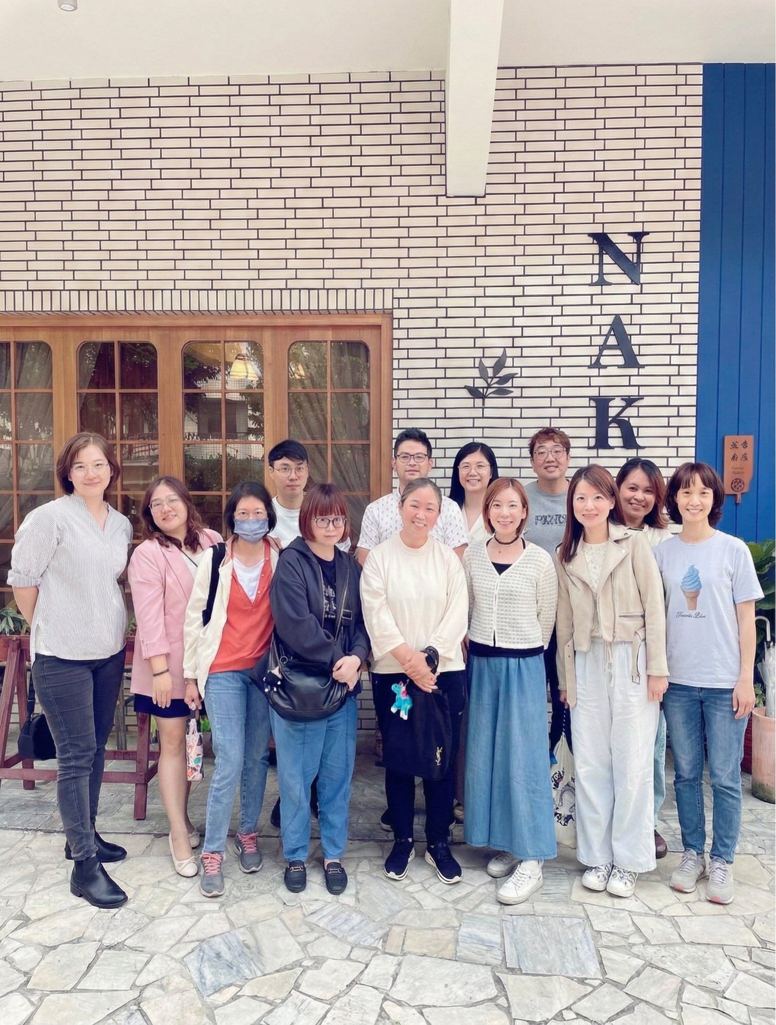 一群人在一棟寫有「NAK」字樣的建築物前擺姿勢拍照。