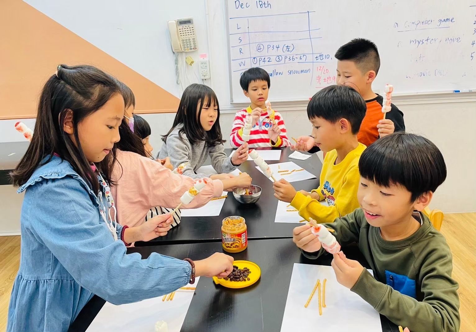 孩子們在桌子旁用小樹枝和一罐棕色的東西做手工。