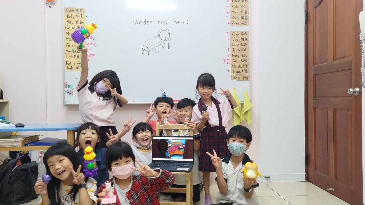 孩子們面帶微笑,擺著各種姿勢拍照,有的戴著口罩,教室裡有白板和筆記型電腦。