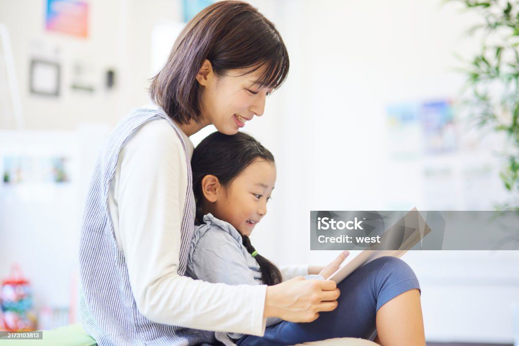 女子和孩子在室內一起用平板電腦看書；兩人都面帶微笑，全神貫注。