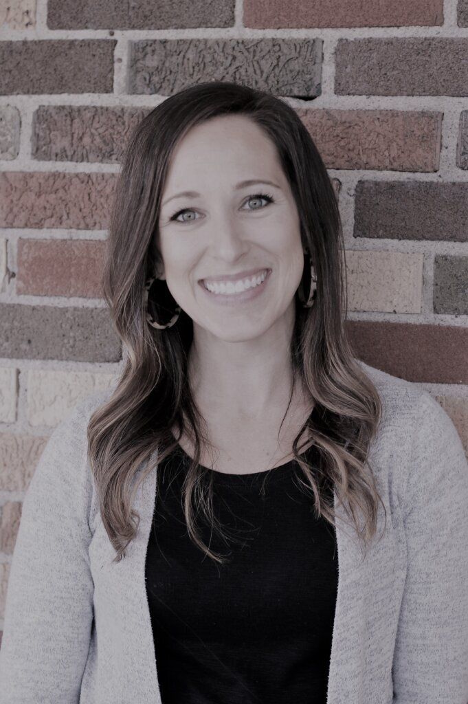 A woman is smiling in front of a brick wall.