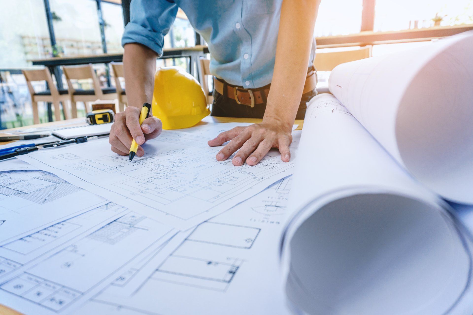 A man is sitting at a table drawing on a blueprint.