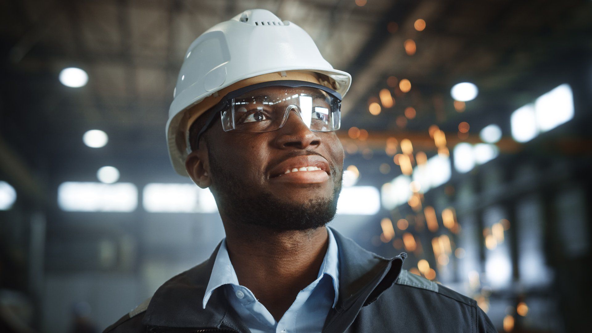 A man wearing a hard hat and safety glasses in a factory.