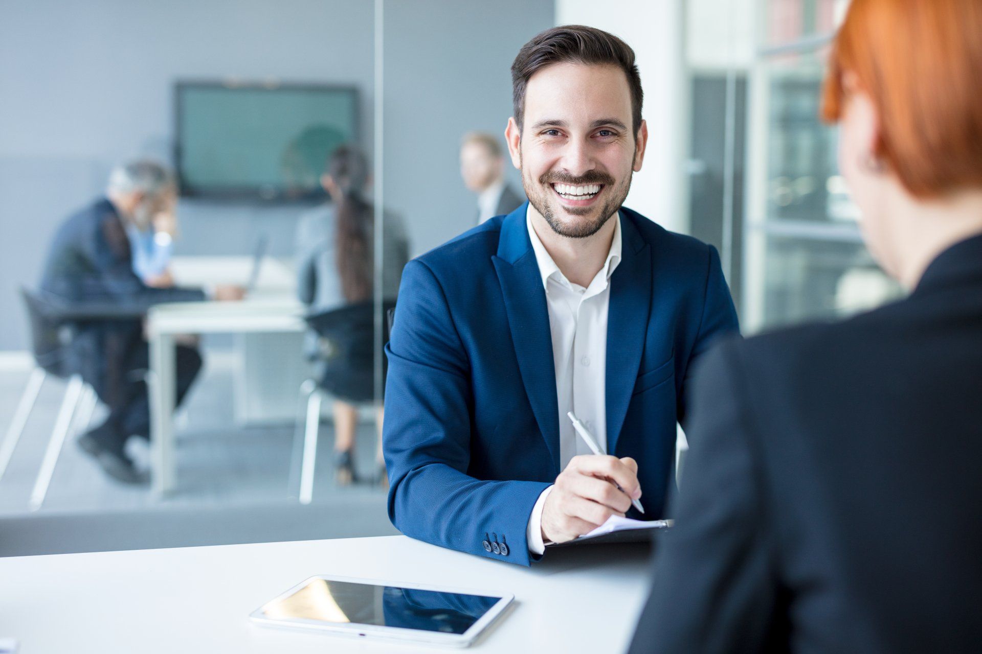 A man in a suit is sitting at a table talking to a woman.