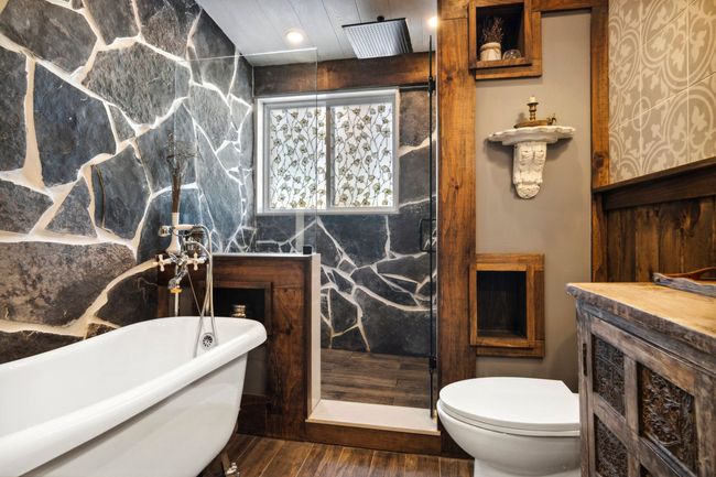 A bathroom with a tub , toilet , sink and stone walls.